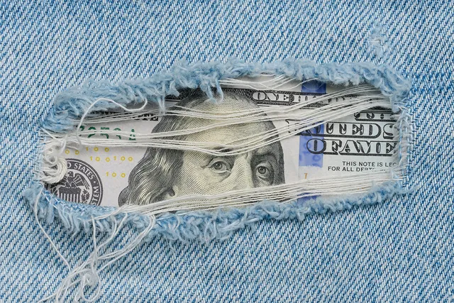 Hundred-dollar bill tucked behind torn denim, a nod to savings