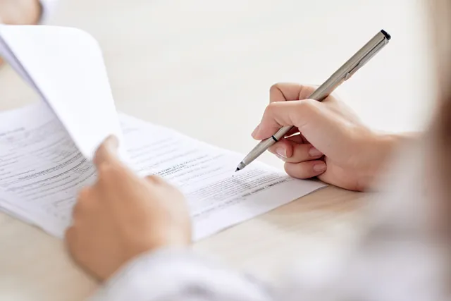 Person signing a document with a pen